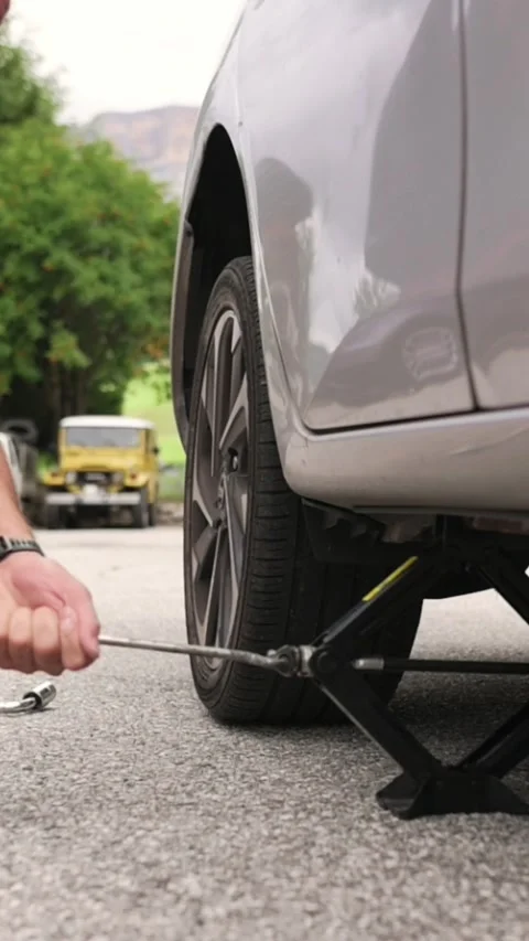 Vertical screen close-up of man using jack and tools to change car tire during Stock Footage 318195188