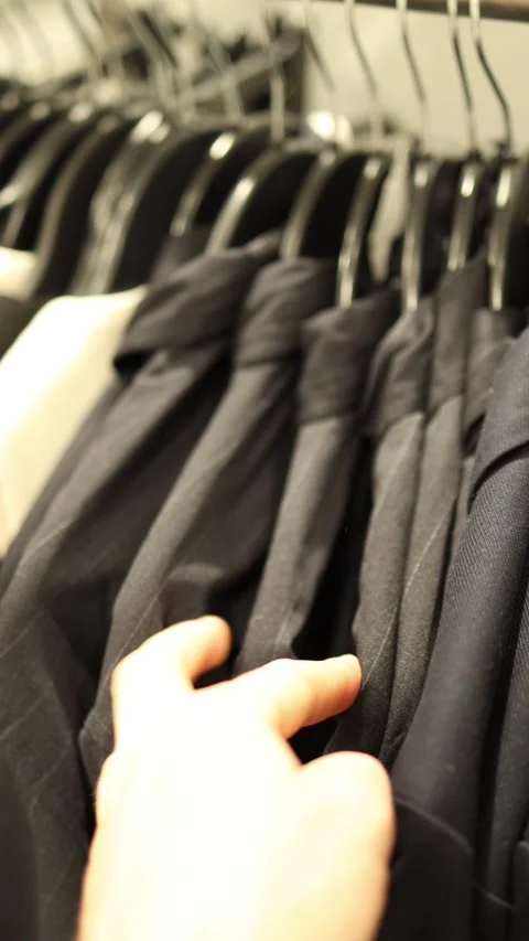 Vertical screen close view of elegant dark suits hanging on rack in fashion stor Stock Footage 317507047