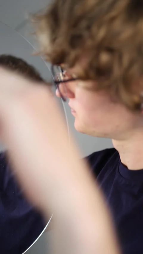 Vertical screen confused and doubtful he stares at his reflection with a tense g Stock Footage 313268943