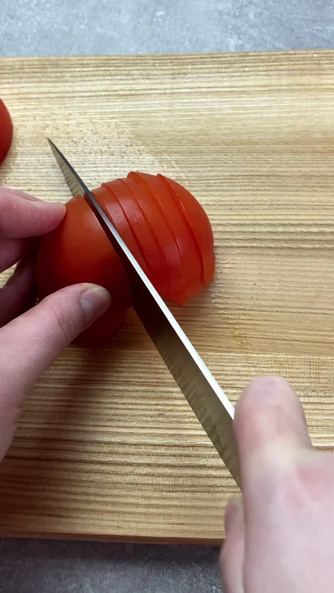Vertical screen: Cook cuts tomato with a large kitchen knife. utting tomatoes Stock Footage 238700676