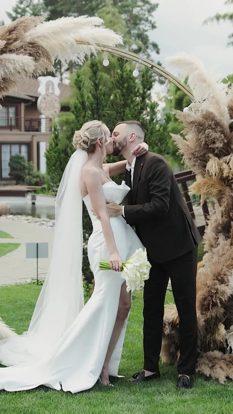 Vertical screen: Couple, bride and groom kissing under wedding arch decorated Video stock 322051179