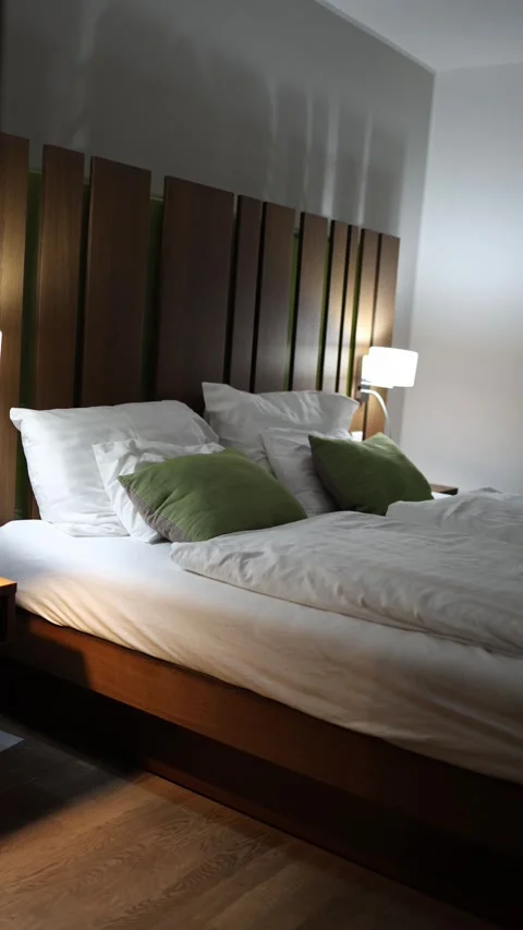 Vertical screen cozy hotel bed with white linens and green pillows illuminated b Stock Footage 318217654