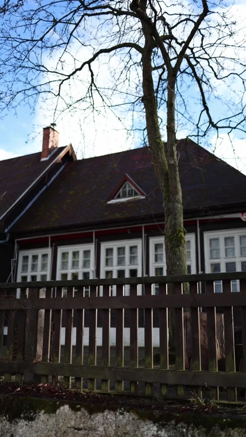 Vertical screen: A cozy house with a dark roof and white trim, seen through a wo Stock Footage 300539776