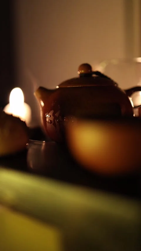 Vertical screen: A cozy scene with a small ceramic teapot, warm candlelight, and Stock Footage 299380745