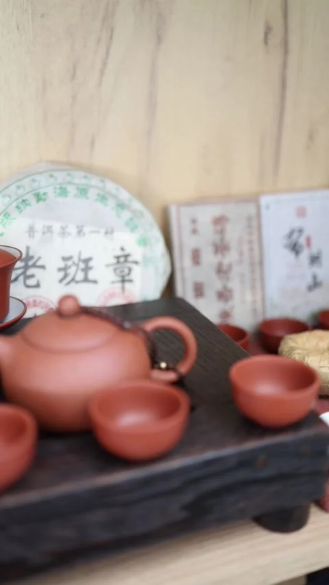 Vertical Screen: A cozy tea corner with clay teapots, cups, and a wrapped Pu-erh Stock Footage 304623019