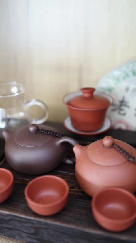 Vertical Screen: A cozy tea scene with a Yixing teapot, clay cups, and a glass p Stock Footage 304623029