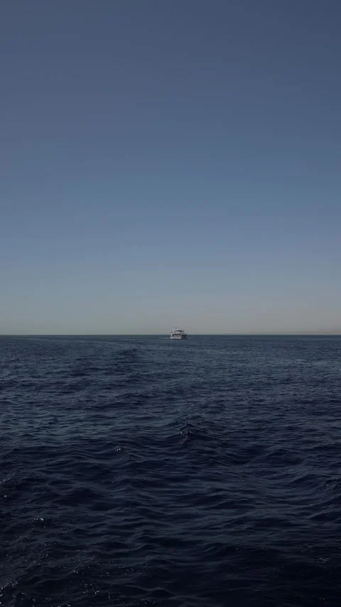 Vertical screen distant yacht sails across dark blue ocean under soft sky empty  Stock Footage 310518389