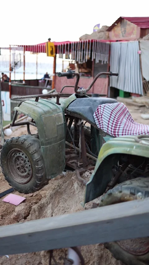 Vertical screen dusty old quad bike with a checkered cloth seat rests on dry rug Stock Footage 310521102