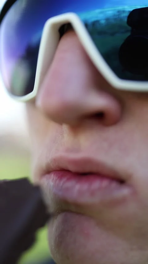Vertical screen. Extreme close-up of a person in sporty sunglasses biting into a Stock Footage 305999145