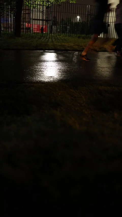Vertical screen: Feet move quickly over the wet asphalt, their reflections shimm Stock Footage 307623151