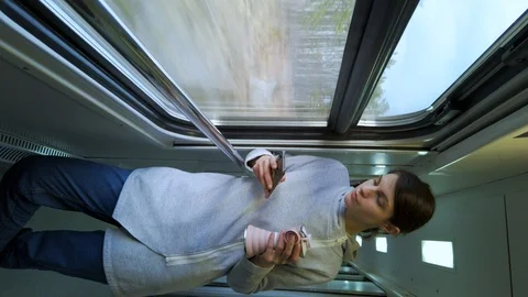 Vertical screen. Female using smartphone. Standing in a train car near window. Stock-Footage 125136087