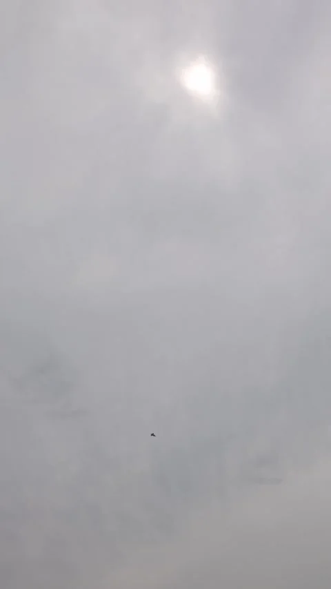Vertical screen fighter jet cuts across pale cloudy sky with diffused sun glowin Stock Footage 311150140