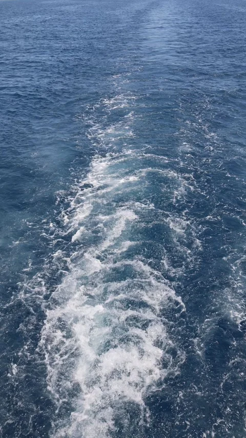 Vertical screen foamy boat trail slices through clear blue sea sparkling in sunl Stock Footage 310518516