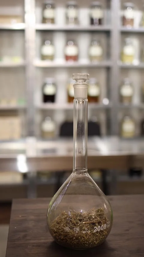 Vertical screen glass laboratory flask with dried herbs inside placed on a woode Stock Footage 317506453