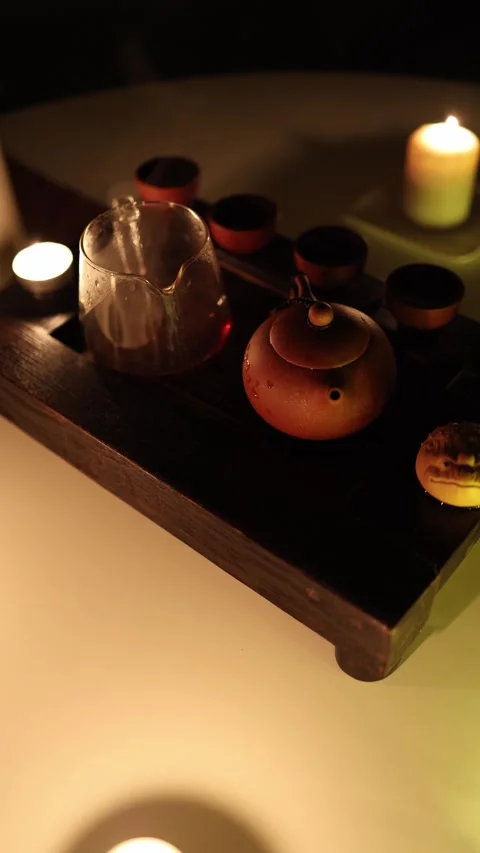 Vertical screen: A gloomy tea setup drenched in dim, suffocating candlelight. Th 스톡 동영상 299379146