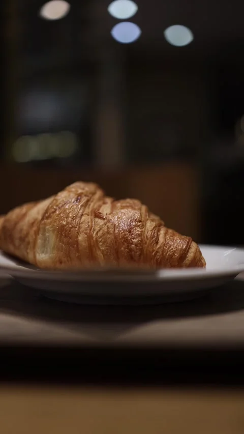 Vertical screen: A golden, flaky croissant resting on a white plate. The soft, w Stock Footage 297264377