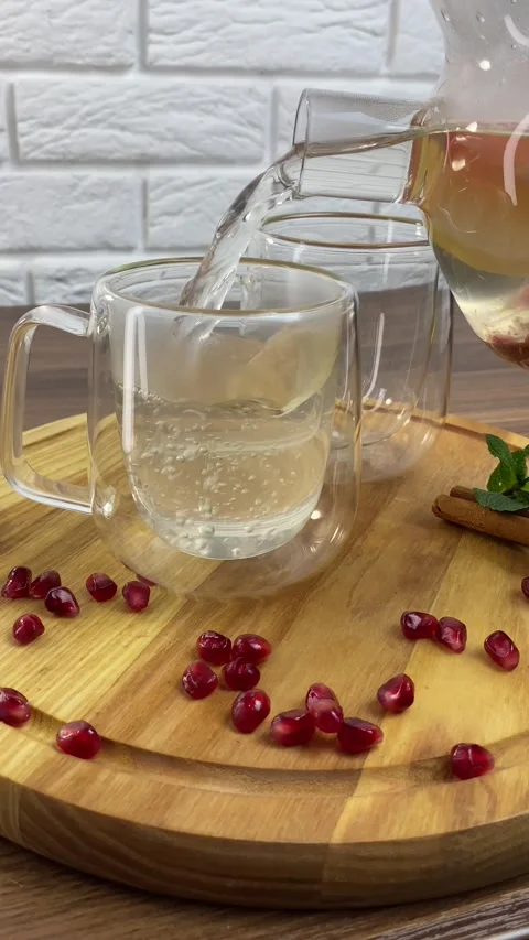 Vertical screen: A hand holding a transparent glass teapot pours hot fruit tea Stock Footage 266149776