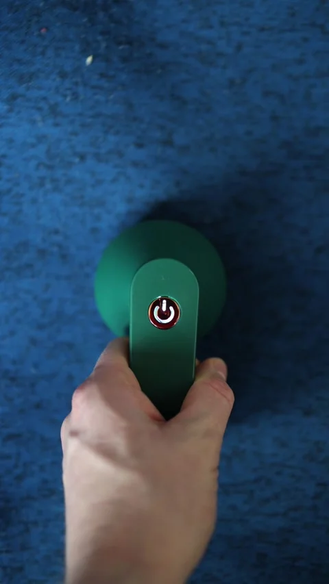 Vertical screen: A hand presses the power button on a green fabric shaver agains Stock Footage 300021668