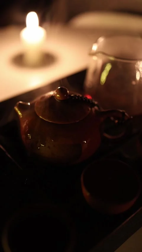 Vertical screen: A handcrafted clay teapot sits near a glowing candle, surrounde Video stock 299380119