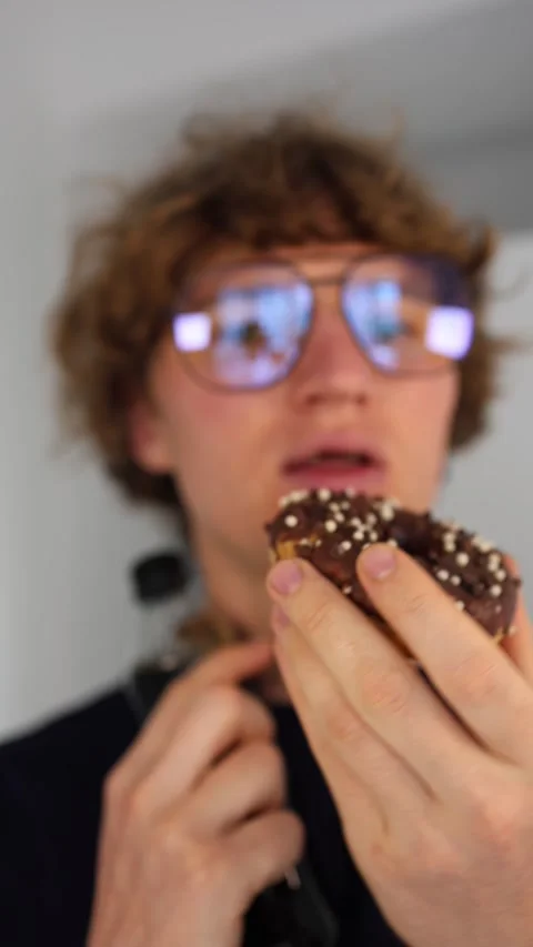Vertical screen holding chocolate donut young man with curly hair and visible de Stock Footage 312195750