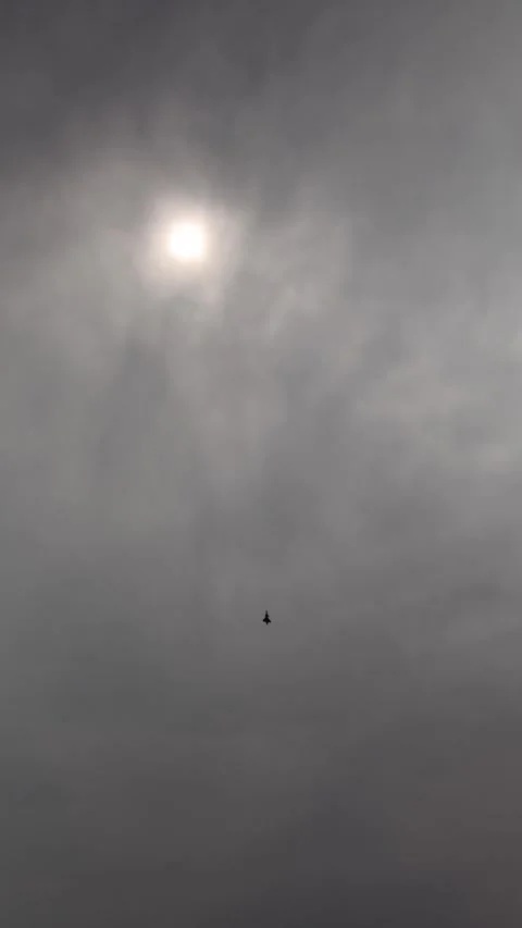 Vertical screen jet fighter cuts through dramatic cloudy sky as diffused sun glo Stock Footage 311150164