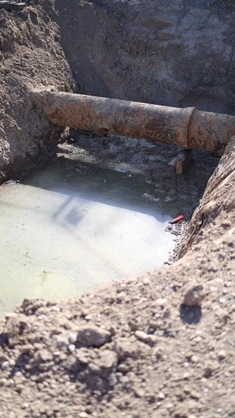 Vertical screen large corroded pipe lies exposed in a muddy construction trench  Video stock 312318042