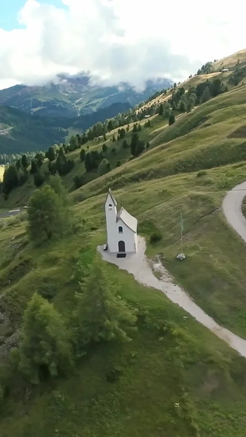 Vertical screen lonely chapel along winding green path rolling meadow, soft Stock Footage 323575436