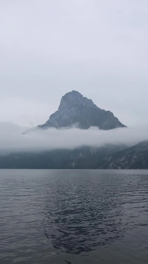 Vertical screen majestic mountain peak rises above calm lake partly covered by l Stock Footage 318217668