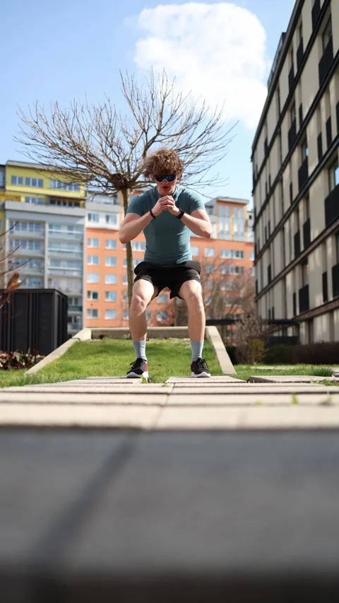 Vertical screen. Man doing deep squats in an urban outdoor setting, focusing on  Stock Footage 305999070