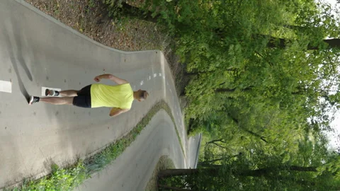 Vertical Screen: Man jogging on empty road between trees Stock Footage 247761750