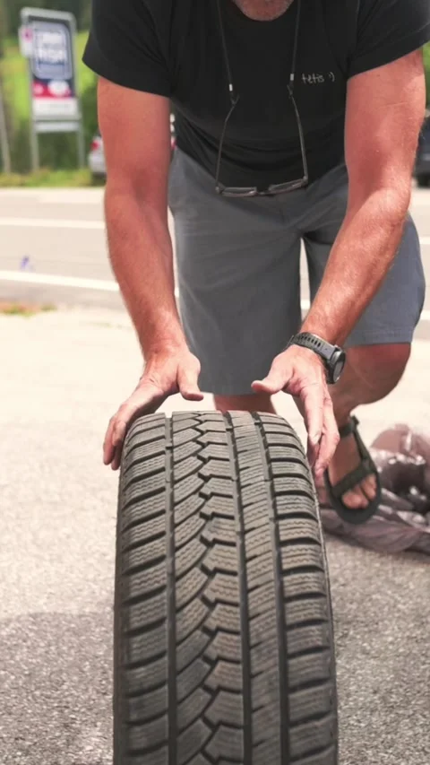 Vertical screen of man lifting a used car tire during roadside replacement Vidéo 318195491