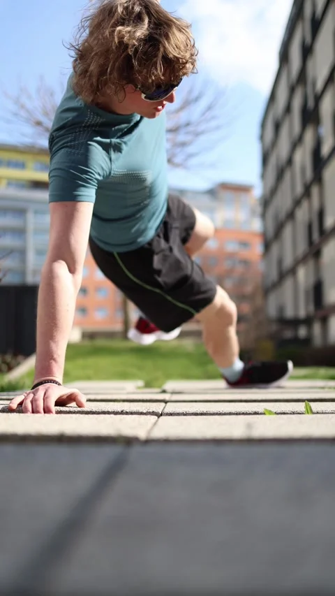Vertical screen. A man performs dynamic side kicks in a plank position outdoors, Video stock 305999079