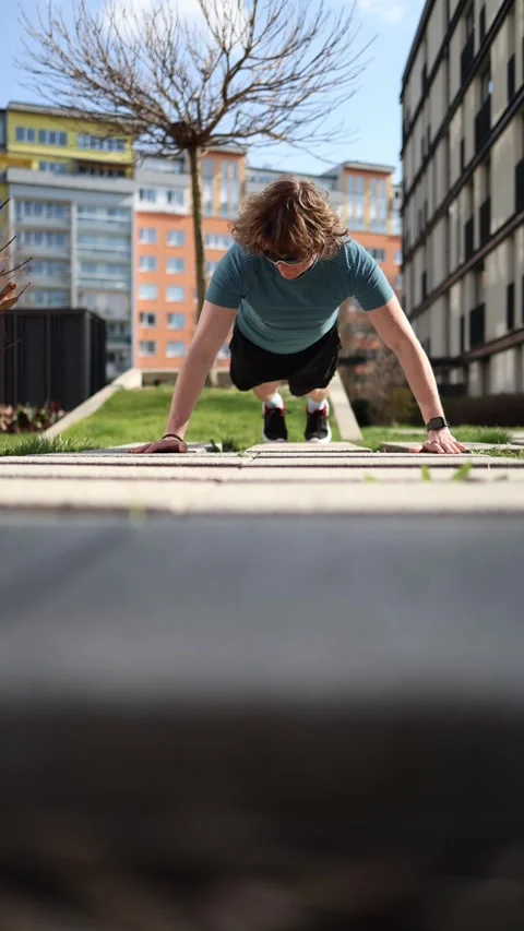 Vertical screen. A man performs one-arm push-ups outside an apartment building,  Vídeos de archivo 305999086