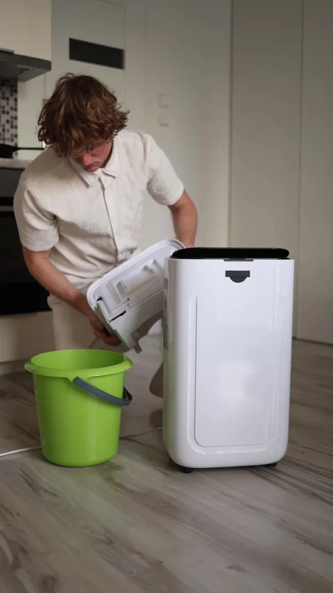 Vertical screen man pours water from dehumidifier tank into green bucket concept Stock Footage 318867709