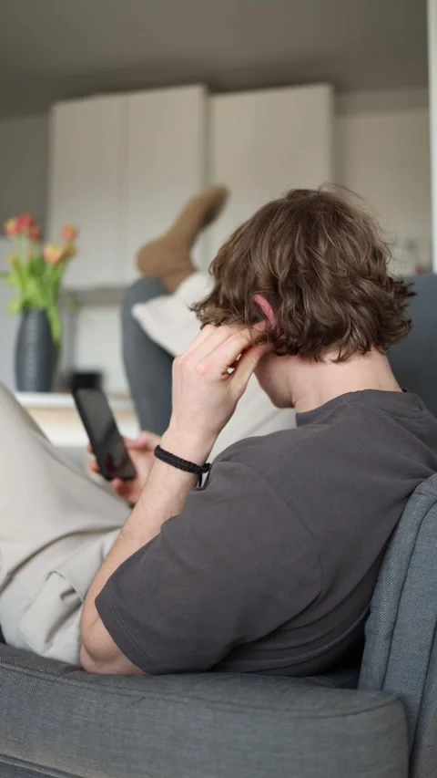 Vertical screen: A man is relaxing on the couch, absorbed in his phone. With his Stock Footage 302633187