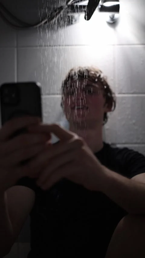 Vertical screen man sits under running shower holding smartphone and smiling whi Stock Footage 316066144