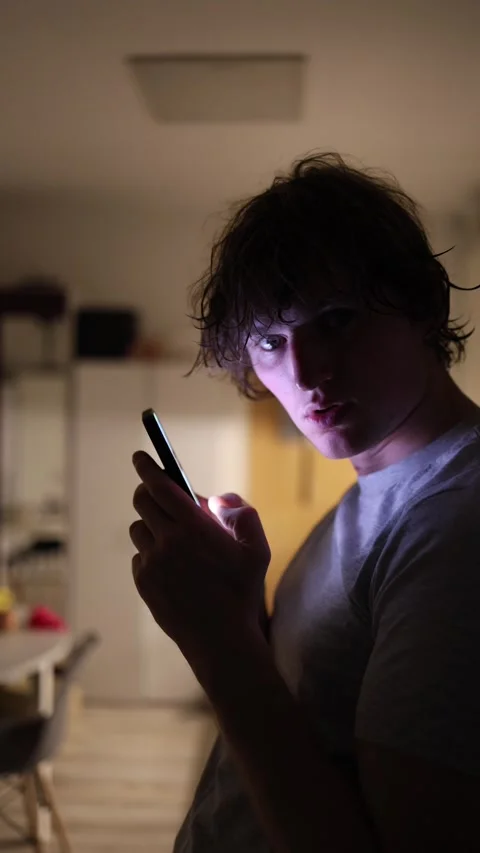 Vertical screen Man turns with surprised expression while holding phone in dim r Stock Footage 313842784