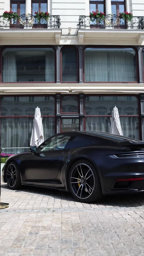 Vertical screen Matte black Porsche sports car parked in front of an elegant his Stock Footage 312676785