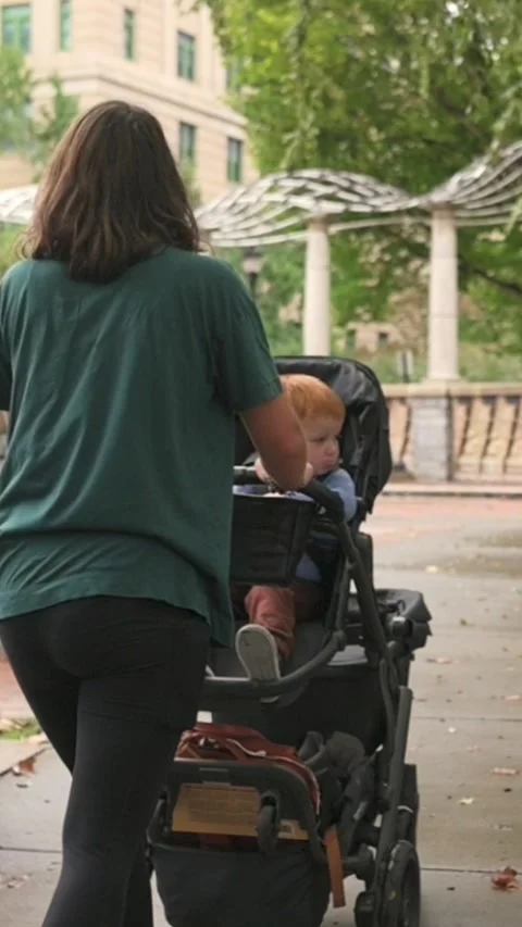 Vertical screen mother checking baby in stroller near open plaza and decorative Stock Footage 323099471
