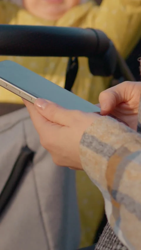 Vertical Screen Mother using smartphone while strolling baby in park Video stock 303564079