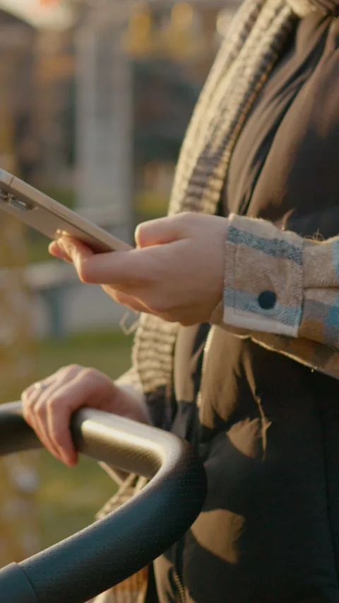 Vertical Screen Mother using smartphone while rocking stroller in park Stock Footage 303564737