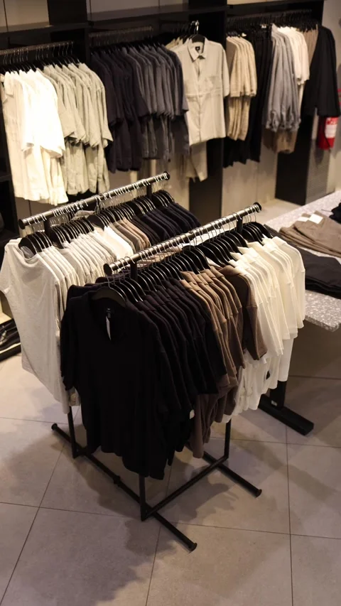 Vertical screen: Neutral-toned shirts neatly arranged on racks in a modern cloth Stock Footage 305175145