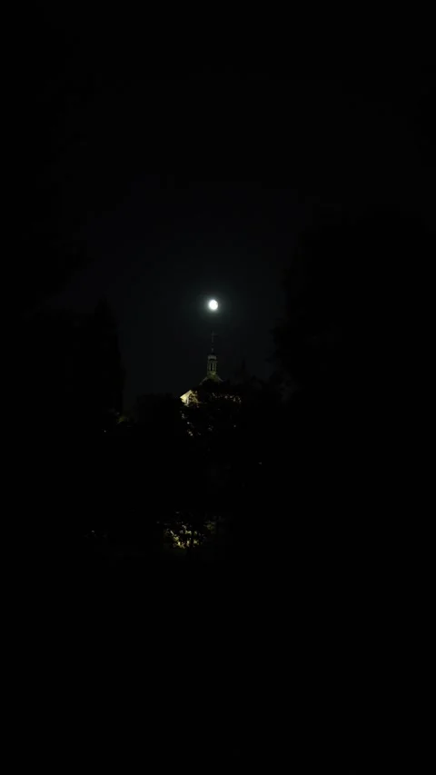 Vertical screen night view with bright moon shining above a tower spire partly h Stock Footage 316700089