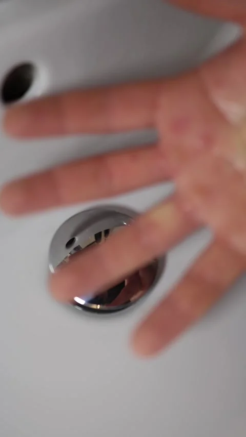 Vertical screen open hand hovers above sink near chrome drain reflection distort Stock Footage 309330267