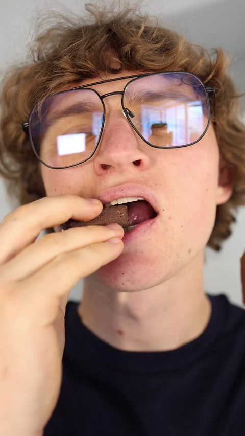Vertical screen overeating sweets a close up of a young man biting into chocolat Stock Footage 312201065