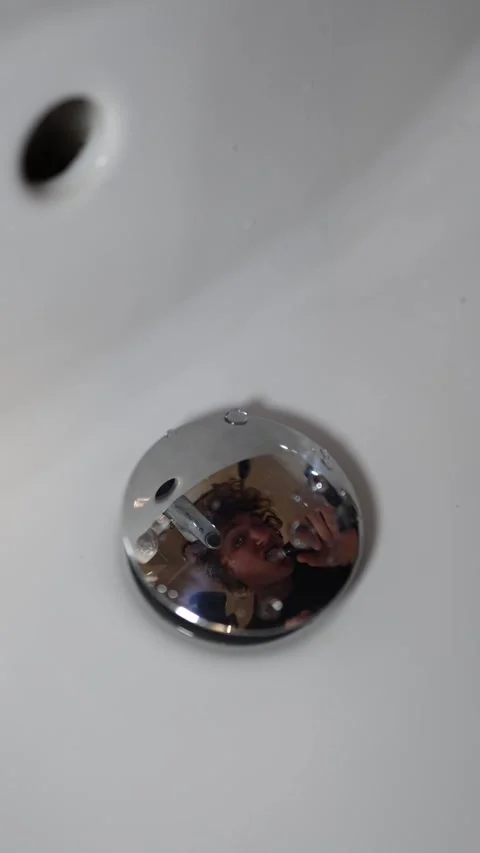 Vertical screen person brushes teeth in front of sink reflection in chrome drain Stock Footage 309329801