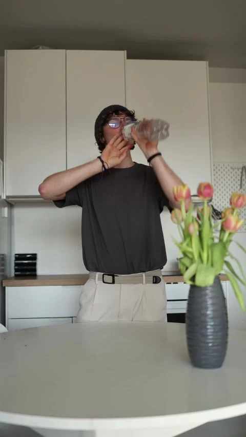 Vertical screen: A person is drinking from a water bottle in a modern kitchen, w Stock Footage 302633436