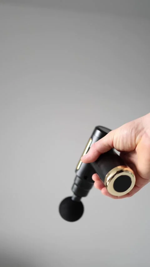 Vertical screen: A person holds a compact massage gun with a sleek black and gol Stock Footage 303907492