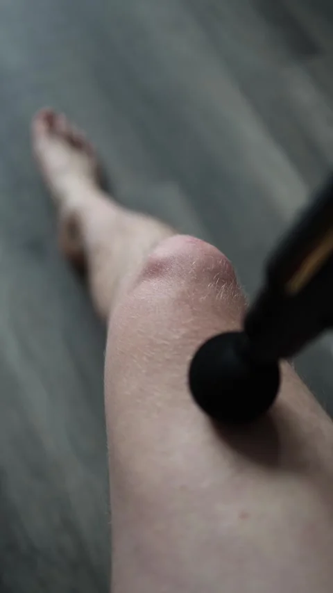 Vertical screen: A person uses a massage gun on their leg, applying deep tissue  Stock Footage 303907506