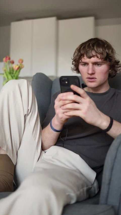 Vertical screen: Pleasantly surprised young man looking intrigued at his smartph Stock Footage 302632408